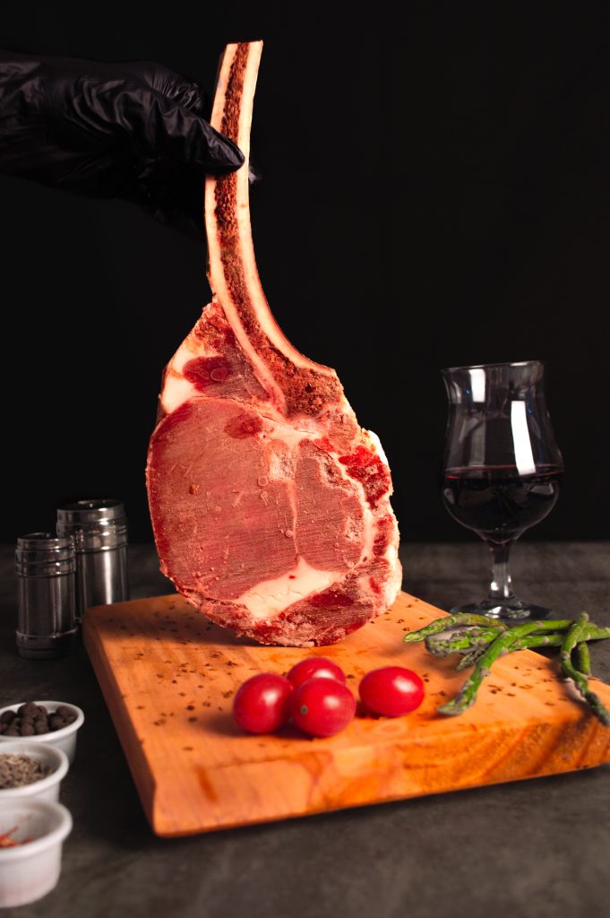 Mano con guante negro sosteniendo brochetas de carne y vegetales sobre un fondo de brasas de carbón encendidas.