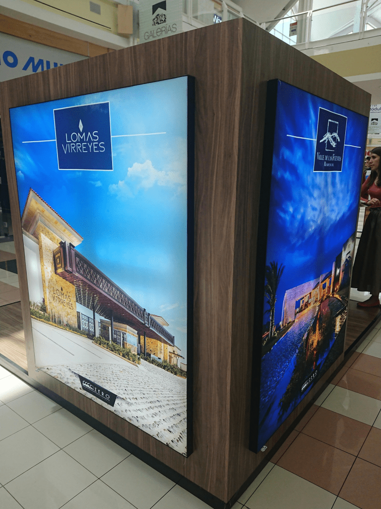 Tótem publicitario de madera con paneles iluminados de Lomas Virreyes y Valle de las Fuentes en un centro comercial.